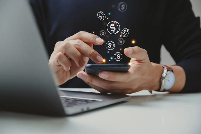 Imagem de uma pessoa mexendo no celular, com ícones digitais de dinheiro flutuando acima da tela