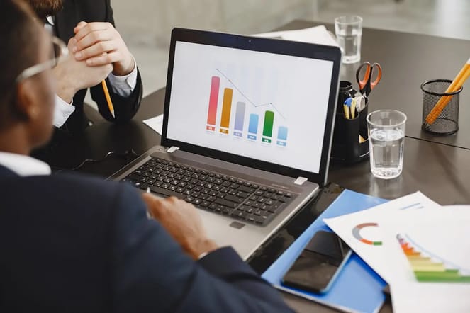 Imagem de pessoas analisando a tela de notebook que mostra um gráfico colorido.