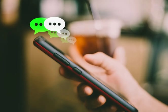 Imagem mostra uma mão segurando um celular e acima dele aparecem ícones que representam balões de conversa.