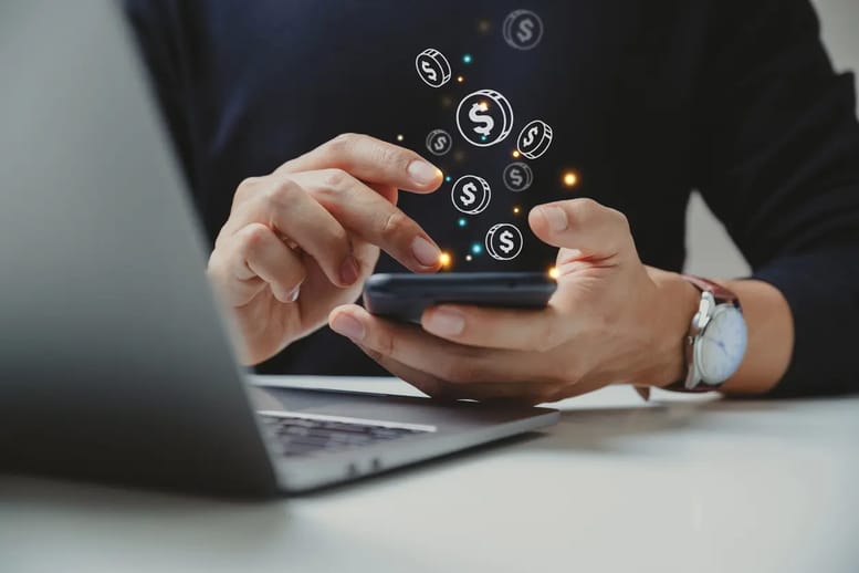 Imagem de uma pessoa mexendo no celular, com ícones digitais de dinheiro flutuando acima da tela