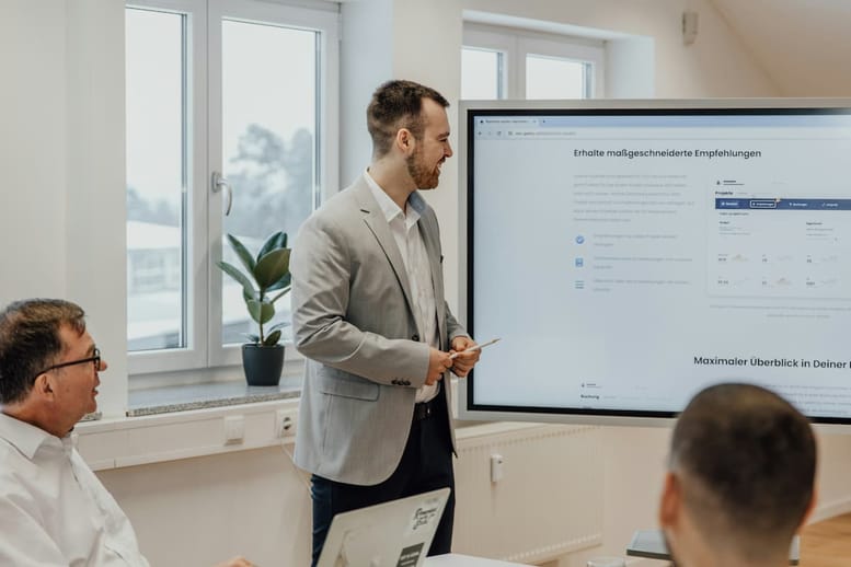Profissionais homens em uma sala de reunião com uma tela com apresentação fazendo gestão de leads.